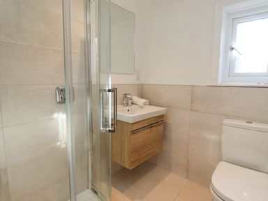 A bathroom with a glass shower enclosure a wall-mounted sink with a wooden cabinet a toilet and a window at The Hollies in Bamburgh