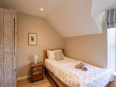 A bedroom with a single bed bedside table lamp wooden wardrobe and a window with striped blind at The Hollies in Bamburgh