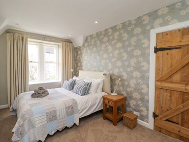 A bedroom with a bed beside a window wooden bedside table and door at The Hollies in Bamburgh