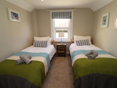 A bedroom with two single beds with striped pillows and blankets with towels on top and a window with a striped blind at The Hollies in Bamburgh