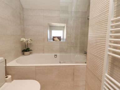 A bathroom with a bathtub a toilet a small window with a basket and a shell and a potted orchid at The Hollies in Bamburgh
