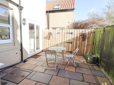 An outdoor patio with a round table and four chairs against a wooden fence at The Hollies in Bamburgh