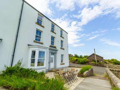 A white multi-story building with a patio table and chairs outside near a road and garden at No6 Sea Lane in Embleton