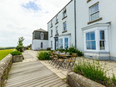 An outdoor patio area with wooden table and chairs next to a white building at No6 Sea Lane in Embleton