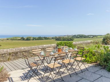 An outdoor patio with wooden tables and chairs overlooking fields and the sea at No6 Sea Lane in Embleton