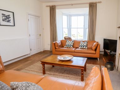 A living room with two leather sofas a wooden coffee table and a bay window at No6 Sea Lane in Embleton