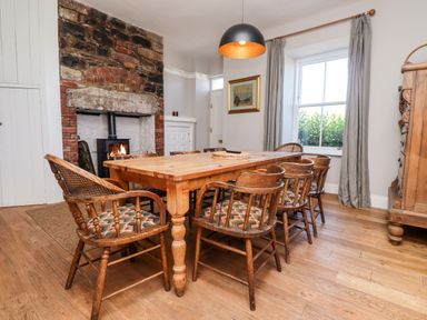 A dining room with a wooden table surrounded by wooden chairs next to a brick fireplace with a fire at No6 Sea Lane in Embleton