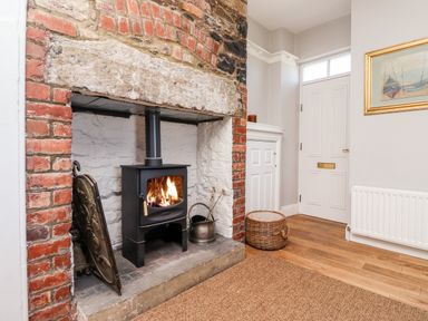 A fireplace with a black wood stove burning and a white door with a wicker basket on a wooden floor at No6 Sea Lane in Embleton