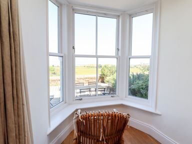 A room with a rattan chair facing a bay window overlooking a garden and fields at No6 Sea Lane in Embleton