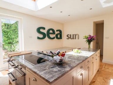 A kitchen island with stove and oven a door leading outside and wall art with the words sea and sun at No6 Sea Lane in Embleton