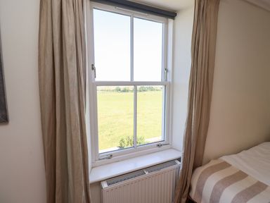 A window with beige curtains next to a bed with a striped blanket at No6 Sea Lane in Embleton