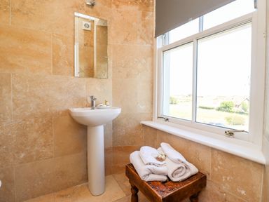 A bathroom with a pedestal sink mirror window and towels on a wooden stool at No6 Sea Lane in Embleton