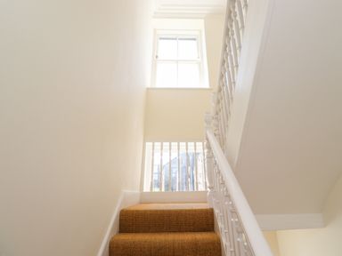 A staircase with brown carpet and white banister with a window at No6 Sea Lane in Embleton