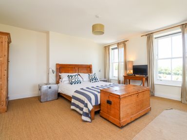 A bedroom with a wooden bed chest windows and a wooden wardrobe at No6 Sea Lane in Embleton