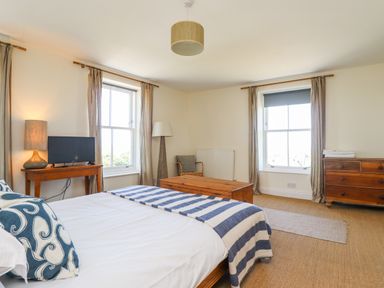 A bedroom with a bed a wooden chest a small table with a lamp and TV a floor lamp a chair and a wooden dresser at No6 Sea Lane Embleton