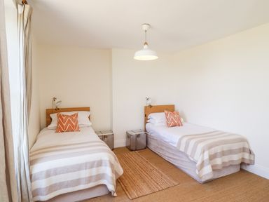 A bedroom with two single beds with striped bedcovers and orange pillows at No6 Sea Lane in Embleton