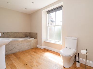 A bathroom with a bathtub tiled with stone panels a white toilet wooden floor and a window at No6 Sea Lane in Embleton