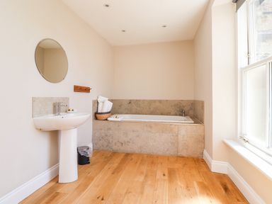 A bathroom with a pedestal sink mirror and bathtub with towels near a window at No6 Sea Lane Embleton