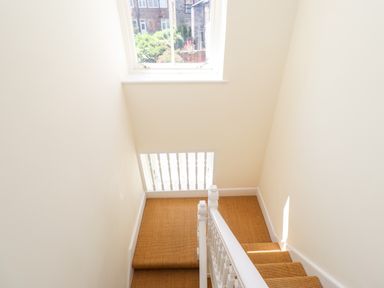A staircase with light brown carpet and white railing with a window above at No6 Sea Lane in Embleton