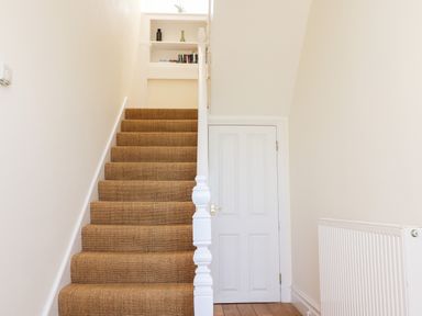 A staircase with brown carpet and a white banister next to a white door and radiator at No6 Sea Lane in Embleton