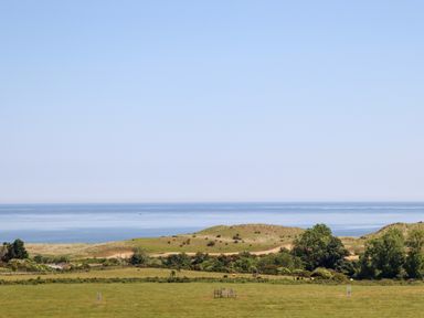 A coastal landscape with green fields trees and hills overlooking the sea at No6 Sea Lane in Embleton