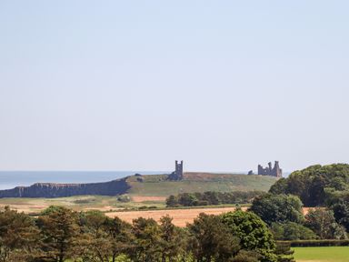 A coastal landscape with ruins on a hill and trees in the foreground at No6 Sea Lane in Embleton