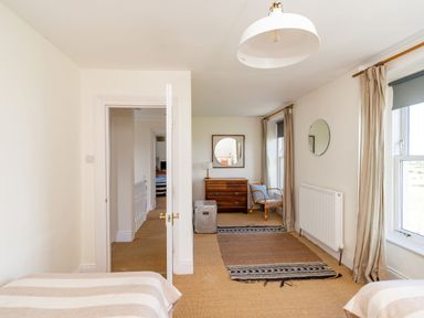 A bedroom with two beds a chest of drawers a chair two windows with curtains and a door at No6 Sea Lane in Embleton