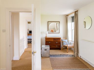 A hallway with a wooden dresser a round mirror a wicker chair and a striped rug at No6 Sea Lane in Embleton