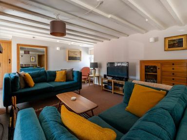 A living room with teal sofas yellow pillows a wooden coffee table a television on a stand and paintings on the wall at The Arches in Bamburgh