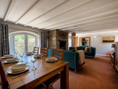 A dining table with dishes and glasses next to a living area with teal sofas and a stone fireplace at The Arches in Bamburgh