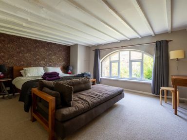 A bedroom with a bed a sofa and an arched window with curtains at The Arches in Bamburgh