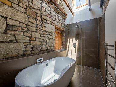 A bathroom with a freestanding bathtub stone wall and walk in shower at The Arches in Bamburgh