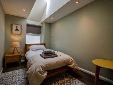 A bedroom with a single bed a lamp on a wooden bedside table a yellow side table and a framed picture on the wall at The Arches in Bamburgh