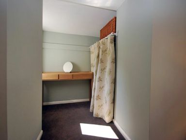 A small room with a wooden desk a round mirror on the desk a floral curtain and a wicker basket on top of the curtain rod