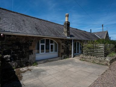 An exterior stone wall with arched windows and a paved patio area at The Arches in Bamburgh