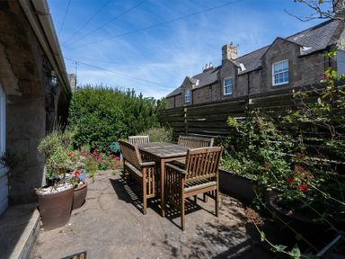 An outdoor patio with wooden table and chairs surrounded by plants and flowers at The Arches in Bamburgh