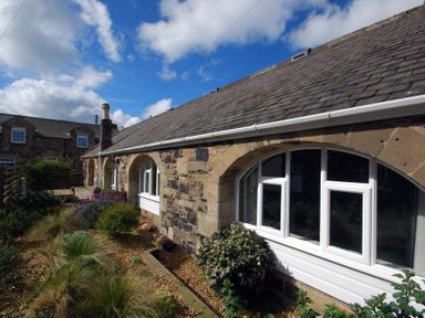 A stone building with arched windows and a garden with plants and flowers at The Arches in Bamburgh