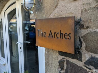 A metal sign reading The Arches mounted on a stone wall near a white door