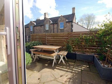An outdoor patio with wooden table and benches surrounded by plants and a wooden fence at The Arches in Bamburgh