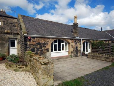 Exterior of a stone house with arched windows and a paved courtyard at The Arches in Bamburgh