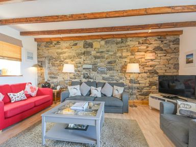 A living room with a red sofa a gray sofa a gray armchair a stone feature wall wooden ceiling beams and a TV at Farne Lookout in Seahouses