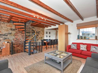 A living area with a red sofa and a gray sofa around a coffee table a spiral staircase and a dining table with chairs at Farne Lookout in Seahouses