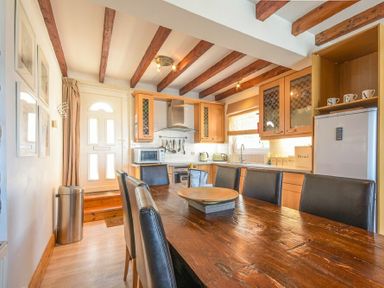 A kitchen with wooden dining table and black chairs wooden cabinets and a white door at Farne Lookout in Seahouses