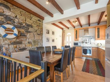 A dining area with a wooden table and black chairs next to a kitchen with wooden cabinets and a tiled wall at Farne Lookout in Seahouses