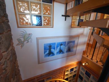 A stairwell with framed lighthouse pictures and mosaic fish art on the wall at Farne Lookout in Seahouses