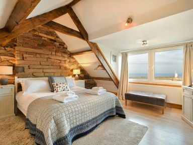 A bedroom with a bed lamps wooden beams and a window overlooking the sea at Farne Lookout in Seahouses