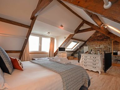 A bedroom with a bed, dresser, TV, wooden ceiling beams, and a stone wall at Farne Lookout in Seahouses