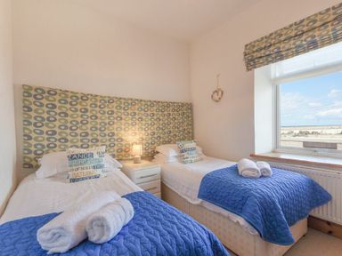 A bedroom with two single beds blue blankets rolled towels patterned headboard and window at Farne Lookout in Seahouses