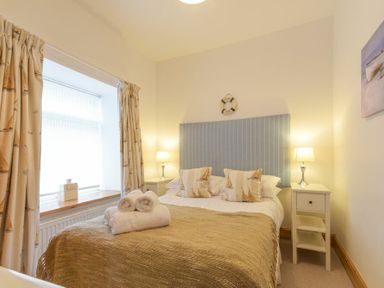 A bedroom with a bed white bedside tables lamps and curtains at Farne Lookout in Seahouses