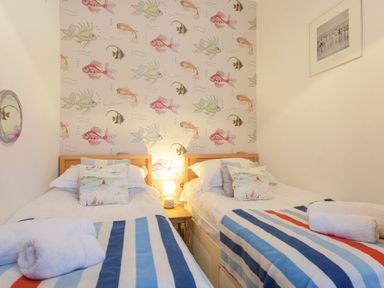 A bedroom with two single beds striped blankets a lamp on a bedside table and fish wallpaper at Farne Lookout in Seahouses
